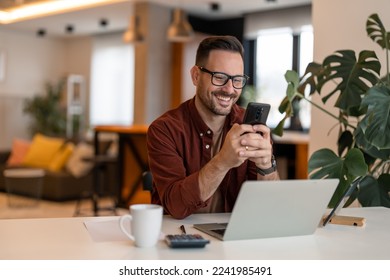 Confident smiling businessman using smartphone in a home office. Checking new e-mails.