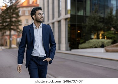 Confident smiling businessman wearing blazer and glasses walking in urban city street. Professional young man enjoying his day. Concept of success, confidence, business attire. - Powered by Shutterstock