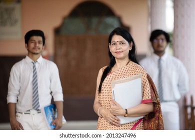 Confident smiling Indian school teacher with students in background - Shutterstock ID 2013247496