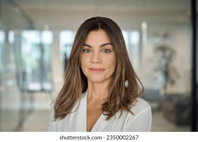 Confident smiling Latin professional mid aged elegant business woman corporate leader, happy beautiful mature female executive, lady manager standing in office looking at camera, headshot portrait.
