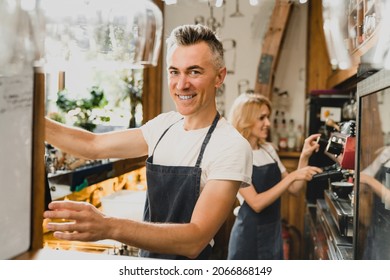 Confident smiling middle-aged small business owners barista bartenders waiters in blue aprons brewing coffee working preparing drinks orders for customers at the bar counter in restaurant cafe.