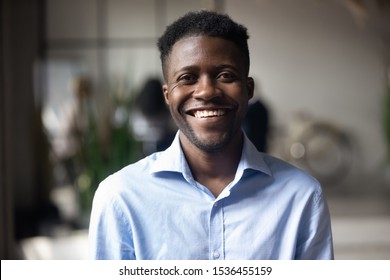 Confident smiling millennial african american businessman looking at camera in modern office, happy male professional company leader coach trainer posing alone, close up head shot business portrait