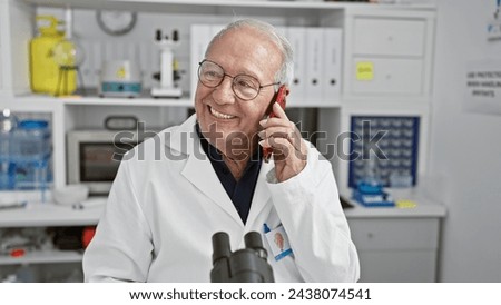 Confident, smiling senior man scientist joyfully engaged in a phone talk, standing in a lab, immersed in profound medical research while smartly working with his trusty smartphone.