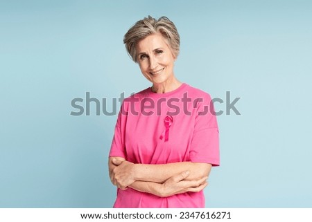 Confident smiling senior woman wearing t shirt with pink ribbon isolated on blue background. Health care, support, prevention. Breast cancer awareness month concept