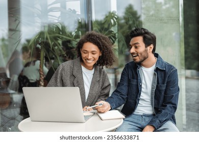 Confident smiling university students studying, learning language using laptop computer, online education concept. Successful Indian man and African American woman working together, planning startup  - Powered by Shutterstock