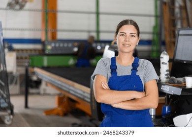 Confident smiling young female worker posing with crossed arms in glass factory, against blurred background of workshop setting, showcasing professionalism and pride in job - Powered by Shutterstock