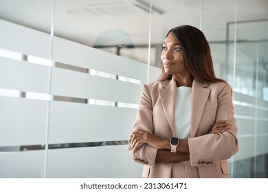 Confident smiling young professional business woman ceo corporate leader, female African American lawyer or manager executive wearing suit standing arms crossed in office, looking away, thinking. - Powered by Shutterstock