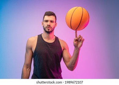 Confident sportsman spinning basketball ball on finger. Young bearded european basketball player looking at camera. Isolated on blue and pink background. Studio shoot. Copy space - Powered by Shutterstock