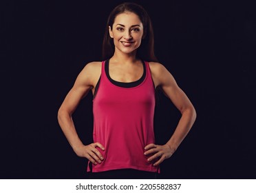 Confident Sportswoman In Pink Sportsbra And Shirt, Holding Hands On Waist, Fitness Trainer Standing In Power Pose, Workout In Gym On Black Background With Empty Copy Space. Toned Color