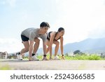 A confident, sporty Asian couple in sportswear is getting ready to sprint on a sunny day in the park. competition, marathon, runners, active lifestyles