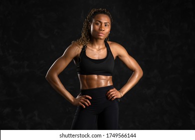 Confident sporty young black African woman portrait, smiling against black background.