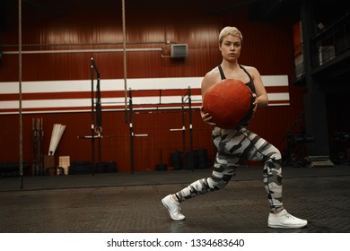 Confident Strong Atheltic Woman With Short Haircut Plunging In Gym, Using Fitness Accessory. Athletic Female In Khaki Outfit Training Core And Arms, Doing Lunge Twist Exercise With Medicine Ball