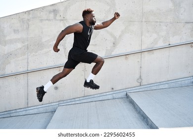 Confident strong fit sporty young black man running along urban wall. Motivated African ethnic guy jumping in air advertising sportswear, street workout training, pursuing goal concept. Side view - Powered by Shutterstock