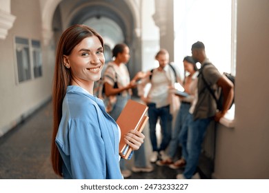 A confident student is depicted in a busy university hallway, holding books among a group of chatting peers, symbolizing the educational, social, and academic aspects of university life - Powered by Shutterstock