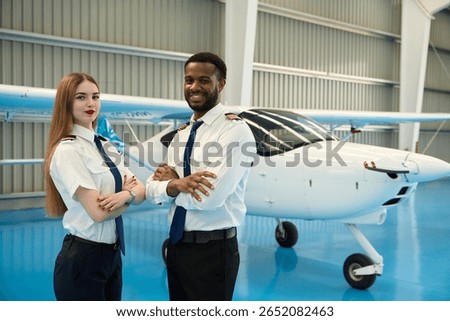 Confident student pilots posing with small airplane in hangar