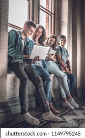 Confident Students.Group Of Happy Young People Working Together And Looking At Laptop While Sitting At The Window Sill Indoors.