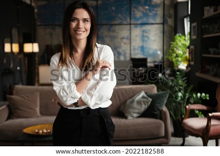 Confident stylish european middle aged woman standing at workplace, 30s lady executive leader manager looking at camera