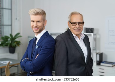 Confident successful business partners posing together with a stylish young man and his older mentor standing back to back smiling at the camera