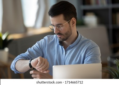 Confident successful businessman checking time, looking at wrist watch, serious young man entrepreneur wearing glasses sitting at desk with laptop, planning work, task management concept - Shutterstock ID 1714665712