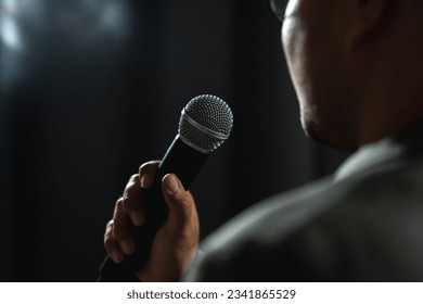 Confident successful speaker man talking on stage with spotlight strike through the darkness at corporate business event. Public speaker giving talk at conference hall. Stand up comedian.