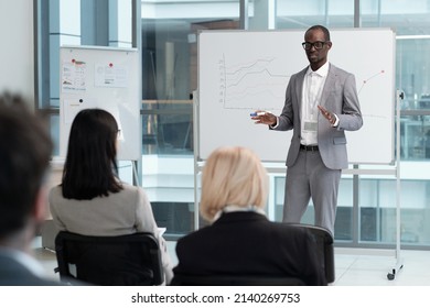 Confident teacher in elegant grey suit explaining audience graphic data on whiteboard during lecture of economics in conference hall - Shutterstock ID 2140269753