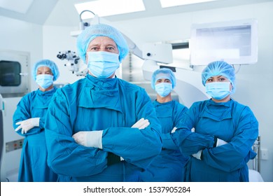 Confident Team Of Surgeons In Scrubs, Caps And Face Masks Standing With Their Arms Folded And Looking At Camera