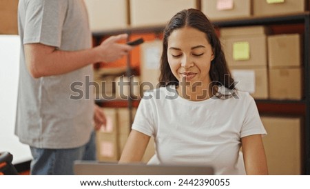 Confident team of two workers, a man and woman, laughing together while working on a laptop in the vibrant office, packaging ecommerce orders for shipping.