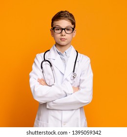 Confident teen boy in doctor uniform posing with arms folded, orange background
