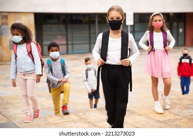 Confident Teen Girl In Protective Mask Walking Outside School Building On Spring Day, Going To Lessons. Concept Of Necessary Precautions In COVID Pandemic.