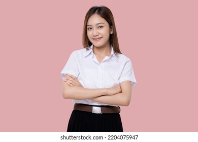 Confident Teen Student Girl Of Asian Ethnicity In University Uniform Crossing Arms Isolated Over Pink Background.