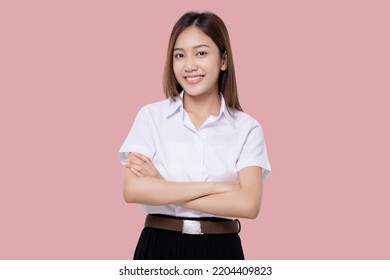 Confident Teen Student Girl Of Asian Ethnicity In University Uniform Crossing Arms Isolated Over Pink Background.