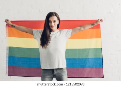 Confident Transgender Woman Holding Pride Flag In Front Of White Brick Wall