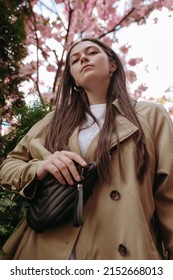 Confident Trendy Woman With Long Brown Hair With Waist Bag Posing And Looking At Camera. Low Angle View Shot