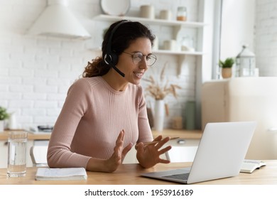 Confident Tutor. Smart Latin Female In Glasses Sit By Laptop At Home Office Provide Video Lesson Explain New Material. Young Lady Expert Interpreter In Modern Headset Work Online Give Teleconsultation