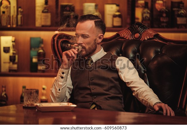 Confident upper class man smoking cigar in\
gentlemen\'s club
