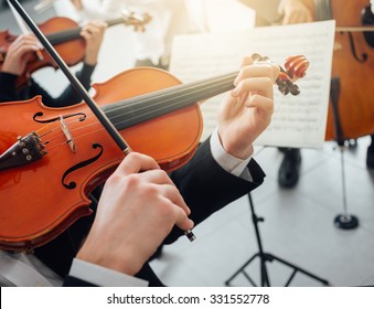 Confident Violinist Playing His Instrument And Reading A Music Sheet, Classical Music Symphony Orchestra Performing On Background