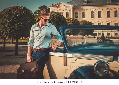 Confident wealthy young man with briefcase near classic convertible 