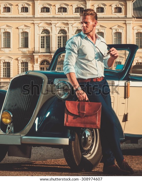 Confident wealthy young man with briefcase near classic
convertible 