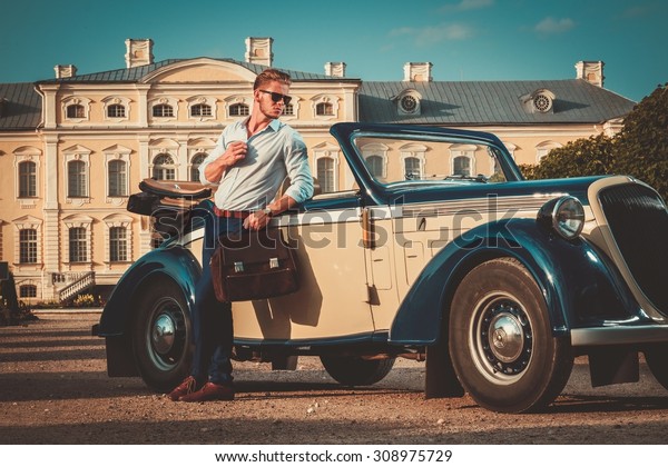 Confident wealthy young man with briefcase near classic
convertible 