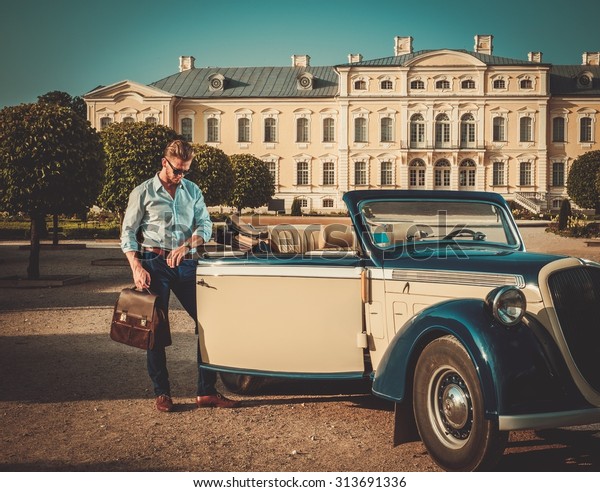 Confident wealthy young man with briefcase near classic\
convertible 