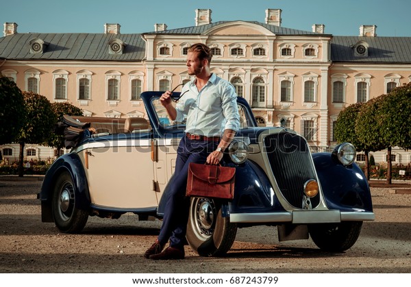 Confident wealthy young man with briefcase\
near classic\
convertible
