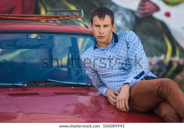 Confident wealthy
young man near old red
car