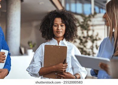 Confident woman with clipboard stands among colleagues during a team meeting in a modern office. Business teamwork and collaboration in a professional environment. - Powered by Shutterstock