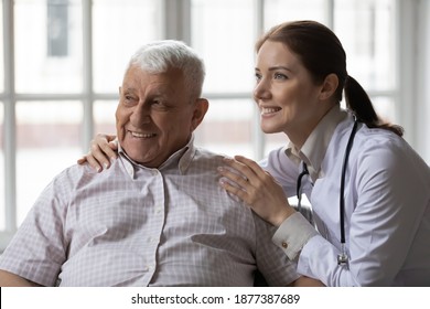 Confident Woman Doctor Hugging Shoulders Of Smiling Retired Male Client Help To Stroke Chronic Diseases. Elderly Male Patient Believe In Good Treatment Result Feeling Support Of Trusted Capable Medic