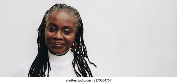 Confident Woman With Dreadlocks Looking At The Camera While Standing Against A White Background. Mature Black Woman Embracing Her Natural Hair.