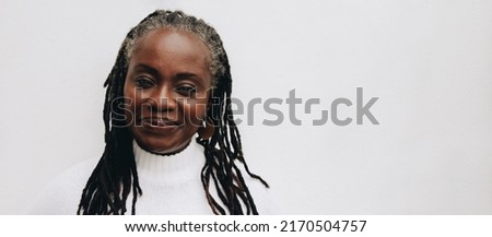 Confident woman with dreadlocks looking at the camera while standing against a white background. Mature black woman embracing her natural hair.