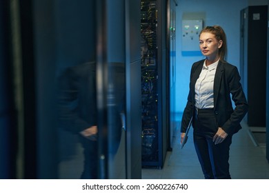 Confident woman engineer standing near server racks in datacenter