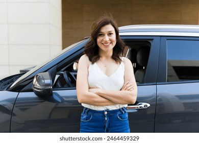 Confident woman in her 30s stands with arms crossed next to her car, radiating joy and readiness to hit the road - Powered by Shutterstock