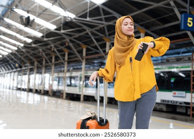 A confident woman in a hijab checks her watch at a bustling train station, ready for travel with her suitcase. The setting reflects modern travel and technology. - Powered by Shutterstock