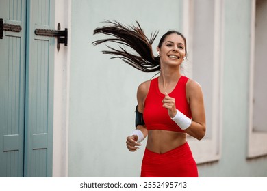 A confident woman jogs outdoors in vibrant red sportswear, embodying energy and joy. Her hair is flowing as she enjoys her fitness routine in an urban setting. - Powered by Shutterstock